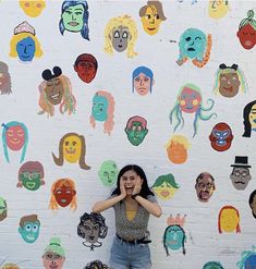 a woman standing in front of a wall with many faces on it