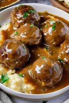 meatballs and gravy in a white bowl on top of mashed potatoes