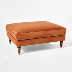 an orange footstool with wooden legs on a white background in front of a plain backdrop