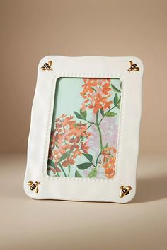 a white frame with orange flowers on the front and bottom, sitting on top of a table