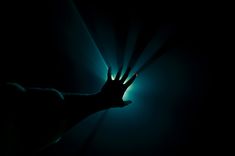 a person's hand reaching up into the air with light coming from behind them