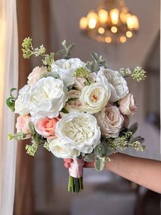 a bridal bouquet being held by someone in front of a window with chandelier