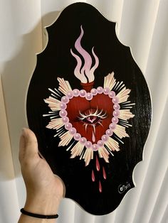 a hand holding up a black and red sign with flames coming out of the heart