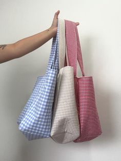 three different colored bags hanging on a wall with one person's hand holding the bag