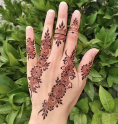 a woman's hand with henna tattoos on it and green leaves in the background