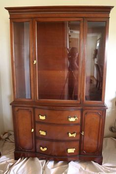 an antique china cabinet with glass doors and gold hardware on the bottom, in front of a white wall