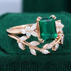 an emerald and diamond ring sitting on top of a green cloth