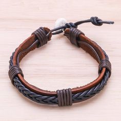 a brown leather bracelet with two braided ends on a wooden surface and a white bead