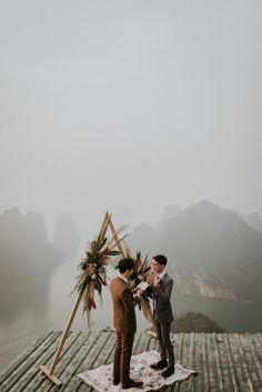 two men standing on top of a wooden dock next to each other holding flowers and looking at each other