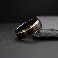 a black and gold wedding ring sitting on top of a rock