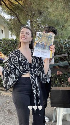 a woman standing in front of a tree holding up a piece of paper with an image on it