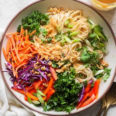 a bowl filled with noodles, carrots and broccoli next to a glass of orange juice