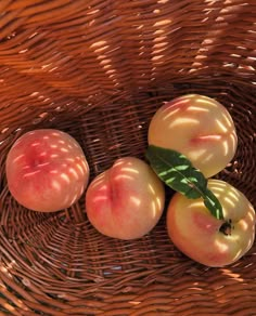 three peaches in a wicker basket with leaves