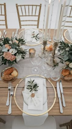 the table is set with white and gold plates, silverware, flowers and candles