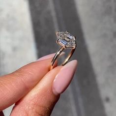 a woman's hand holding an engagement ring in front of her face, with the diamond on it