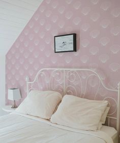 a white bed sitting under a pink wallpaper next to a night stand and lamp