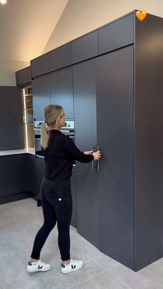 a woman in black shirt and leggings opening the door to a gray kitchen