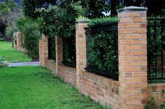 a brick wall with black iron fence and green grass