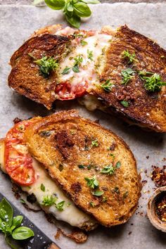 two grilled cheese sandwiches with tomatoes and basil on the side next to a knife