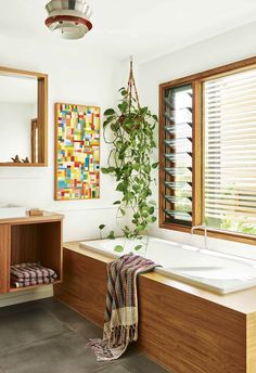 a bathroom with a bathtub, sink and window covered in blinds next to a potted plant