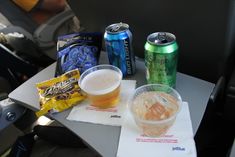 two cans of beer and some snacks on a table in the back seat of an airplane