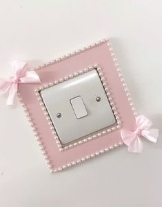 a pink and white light switch cover with bows on the side, sitting in front of a white wall