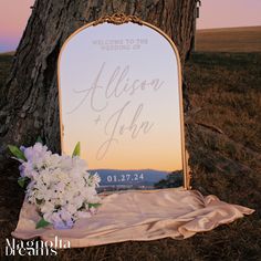 a wedding sign sitting on top of a tree next to a white flower bouquet in front of a mirror