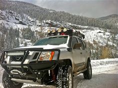 a white truck parked on top of a snow covered road next to trees and mountains