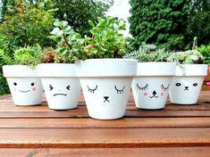 four pots with faces painted on them are sitting on a wooden table in front of some plants