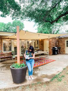 a woman standing next to a potted plant in front of a house on a patio