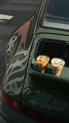 two cups of coffee are placed on the hood of a green car with camouflage paint