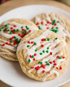 three cookies with white icing and sprinkles on a plate