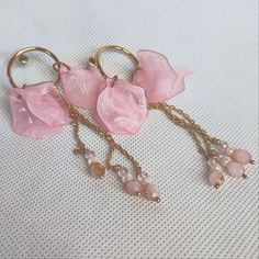 three pink earrings with gold chains and dangling beads on a white tablecloth background,