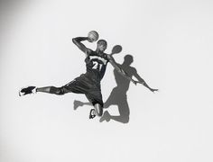 two people playing basketball in the air with their shadows on the wall and one person jumping up to catch the ball