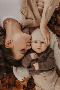 a woman holding a baby in her arms while laying on the ground with autumn leaves