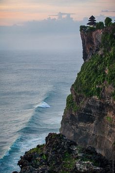 an ocean cliff with a small hut on it's top and waves crashing in the water