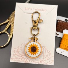 a yellow sunflower keychain hanging from a card next to scissors and thread