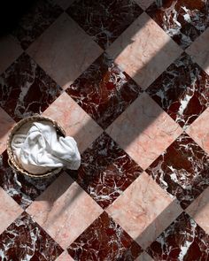 a white and brown basket sitting on top of a checkerboard floor next to a toilet paper roll