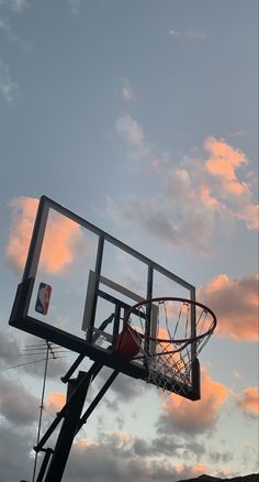 a basketball hoop with the sun setting in the background and clouds above it, as seen from below