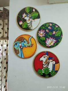 four colorfully painted coasters are hanging on the wall