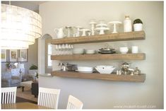 two wooden shelves filled with dishes on top of a wall next to a table and chairs