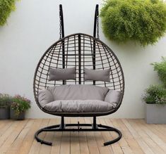 a swing chair with cushions on it in front of some potted plants