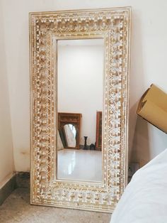 a large mirror sitting on top of a floor next to a white bed in a room