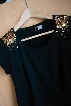 a black shirt with gold sequins on it sitting on a wooden hanger