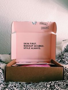 an open box on top of a bed that says skin first, make up second, smile always