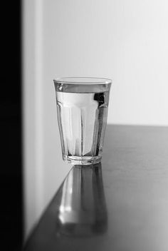 a glass sitting on top of a table next to a wall and window sill