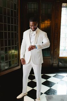 a man in a white tuxedo standing on a black and white checkered floor