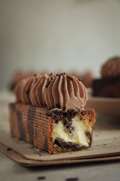 a piece of cake with chocolate frosting on it sitting on a plate next to another cupcake