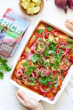 A colorful vegan rice casserole topped with avocado, cherry tomatoes, red onion, cilantro, and seeds. A packet of lotus foods' organic red rice is beside it.