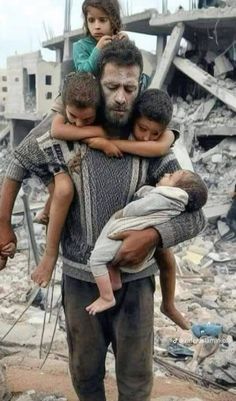 a man holding two children in his arms while standing next to a pile of rubble